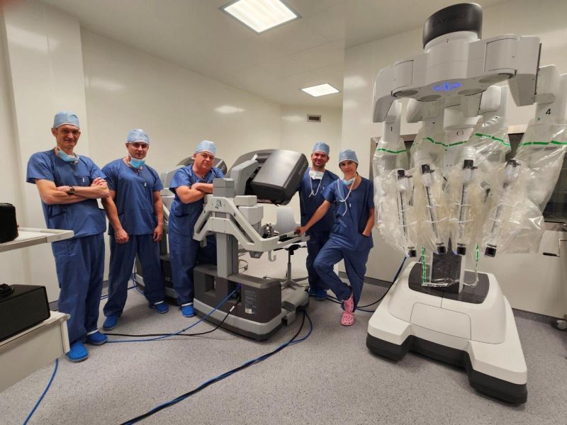 Grupa pięciu chirurgów w niebieskich strojach operacyjnych pozuje we wnętrzu nowoczesnej sali operacyjnej przy stanowisku robota chirurgicznego da Vinci. Lekarze stoją obok konsoli sterującej oraz wieloramiennego robota przygotowanego do zabiegów, co podkreśla praktyczny charakter spotkania Klubu Robotycznego w Wojewódzkim Szpitalu Specjalistycznym w Lublinie.