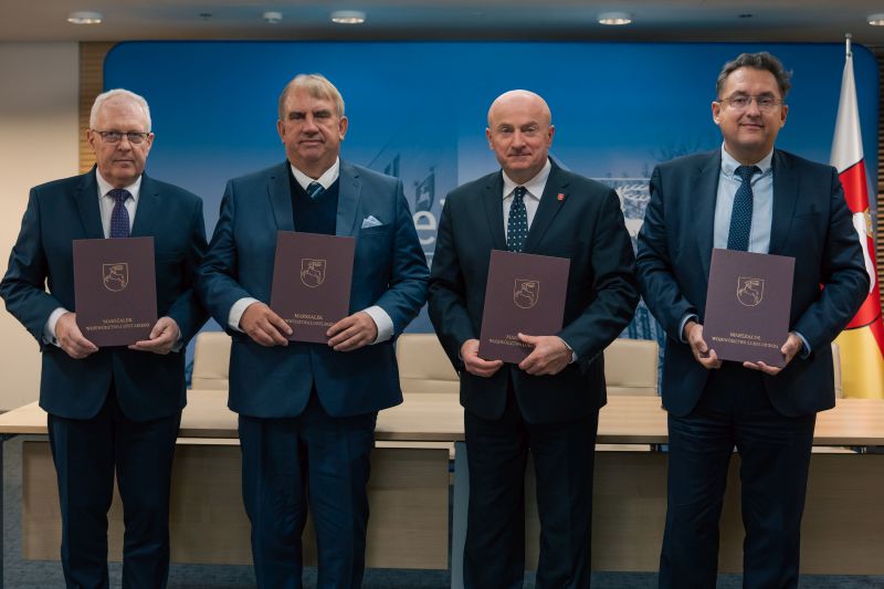 Na zdjęciu cztery osoby stoją w szeregu podczas oficjalnej uroczystości, każda trzyma teczkę z herbem Województwa Lubelskiego i napisem "Marszałek Województwa Lubelskiego". Od lewej: Piotr Matej, dyrektor Wojewódzkiego Szpitala Specjalistycznego im. Stefana Kardynała Wyszyńskiego w Lublinie; prof. dr hab. n. med. Wojciech Załuska, Rektor Uniwersytetu Medycznego w Lublinie; Jarosław Stawiarski, Marszałek Województwa Lubelskiego; Michał Szabelski, dyrektor Uniwersyteckiego Szpitala Klinicznego Nr 4 w Lublinie. Zdjęcie wykonano w sali konferencyjnej podczas podpisania porozumienia o współpracy.