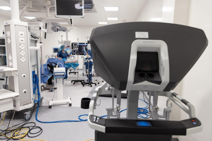 Konsola sterowania robotem daVinci, a w tle sala operacyjna.